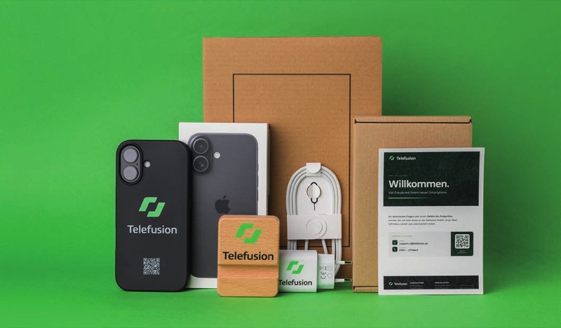 Smartphone mit Telefusion-Case, Verpackung, Netzteil und Willkommenskarte vor grünem Hintergrund